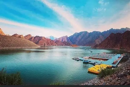 Turquoise water of Hatta Dam with a floating pier of kayaks and pedal boats, surrounded by the rocky Hajar Mountains