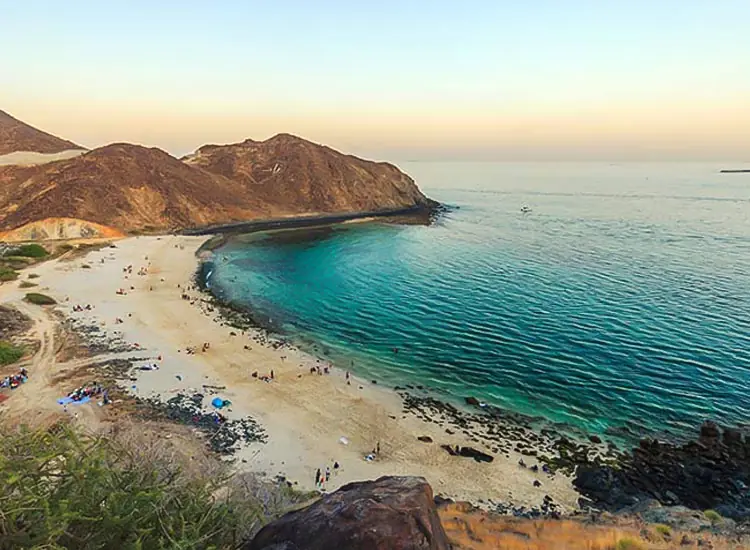 Sandy beach curving around a turquoise cove beneath rocky mountains on the UAE east coast at sunset