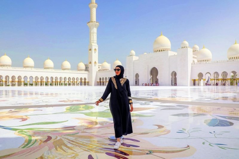 A visitor in an abaya and headscarf in the marble courtyard of the Sheikh Zayed Grand Mosque, Abu Dhabi