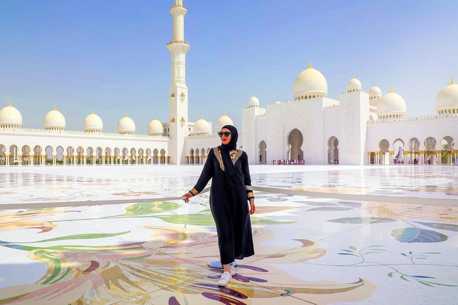 A visitor in an abaya and headscarf in the marble courtyard of the Sheikh Zayed Grand Mosque, Abu Dhabi