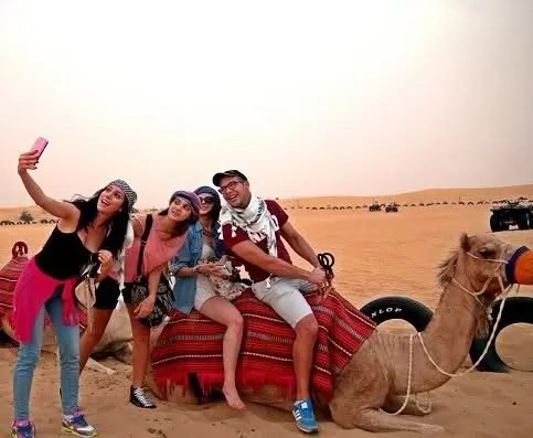 Group of friends taking a selfie while sitting on a resting camel during a Dubai desert safari